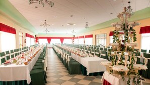 Une salle de banquet avec de longues tables dressées pour un événement formel, agrémentée d’une pièce décorative centrale et de chaises vertes.