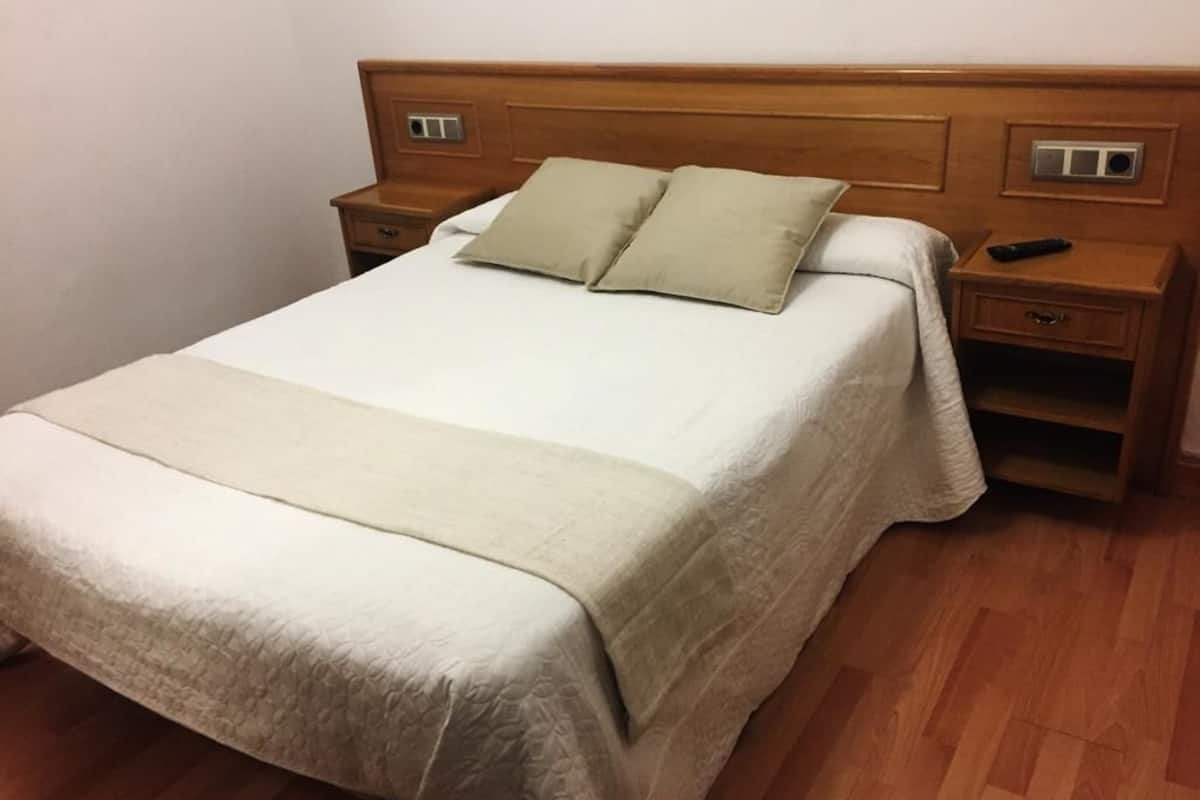 Una cama bien hecha con un cabecero de madera, dos mesitas de noche y un control remoto sobre una de ellas.