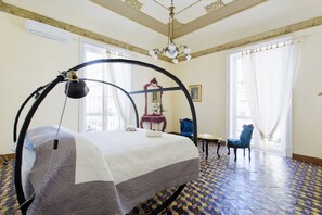 Una habitación con una cama bajo una estructura circular, una araña, una silla azul y un suelo con diseño.