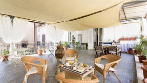 An outdoor patio with wicker furniture, a table set with breakfast, and potted plants. - Artisan Maison (Palermo)
