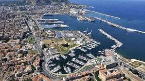 An aerial view of a coastal city with a marina, buildings, and a prominent mountain in the background. - Artisan Maison (Palermo)