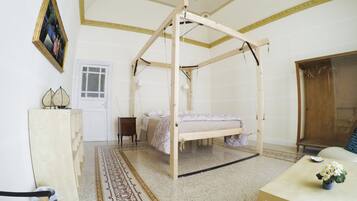 Ein Zimmer mit einem hölzernen Baldachinbett, einem kleinen Tisch mit Blumen, einem Stuhl, einem Schreibtisch und einem gerahmten Bild an der Wand.