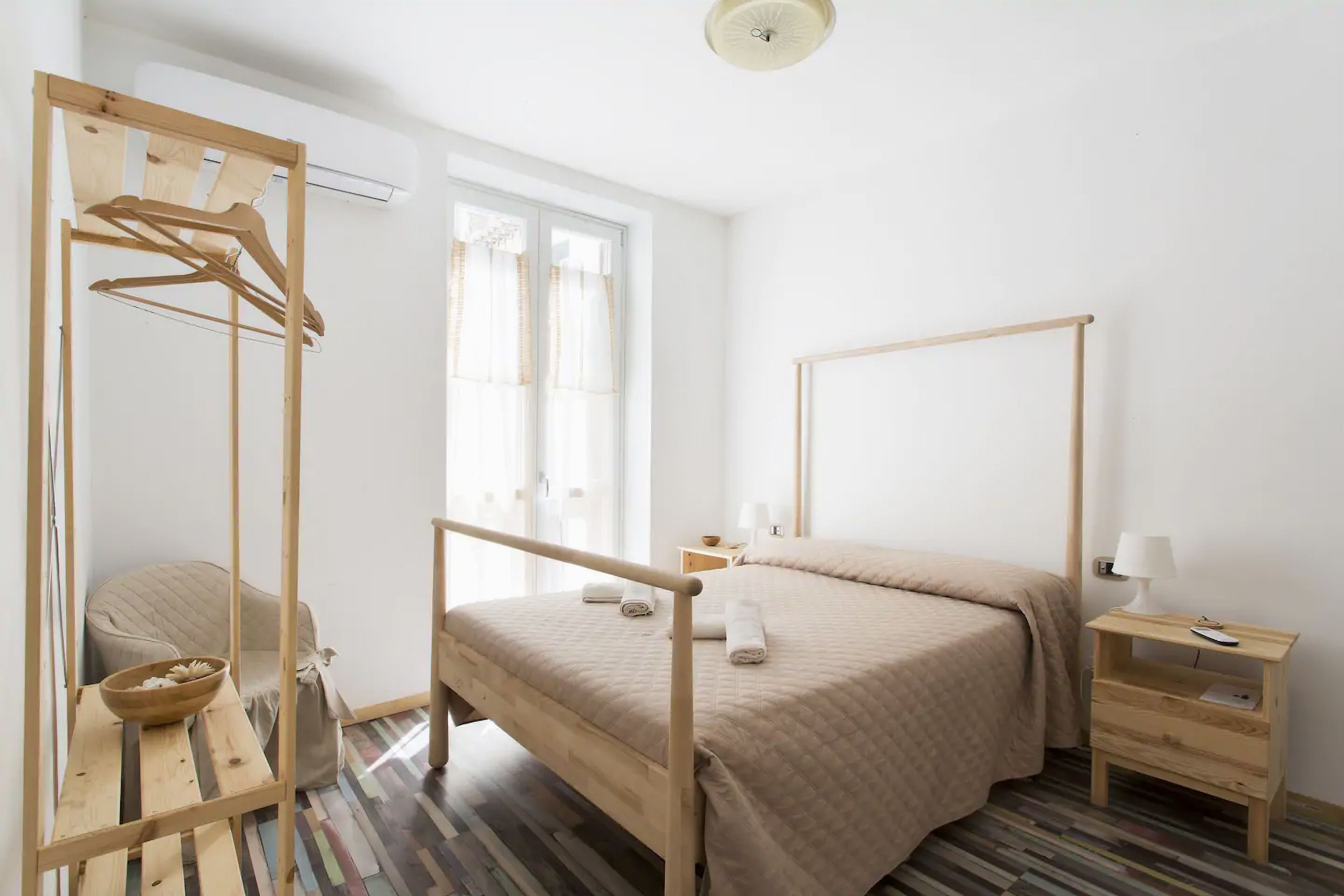 Une chambre à coucher au style minimaliste, avec un cadre de lit en bois, une table de chevet avec une lampe, une étagère suspendue en bois et une chaise.