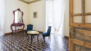 A room with a patterned floor, a round table, two chairs, a purple console table, a mirror, and a wooden door. - Artisan Maison (Palermo)