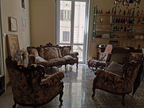 Un salón espacioso con muebles ornamentados, un ventanal grande y una colección de vinos en estanterías.