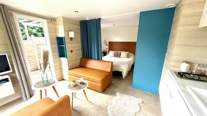 A hotel room with a bed, a sofa, a small table, a TV, and a kitchen area with a stove. - Camping du Manoir de Penn ar Ster (La Foret-Fouesnant)