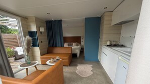 A compact hotel room with a kitchenette, a bed, a seating area, and a view through a sliding door. - Camping du Manoir de Penn ar Ster (La Foret-Fouesnant)
