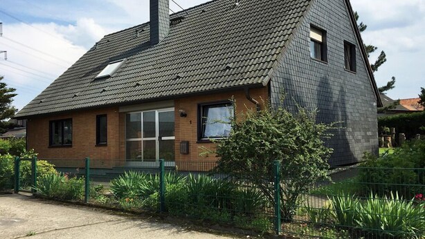Una casa de dos pisos con techo inclinado, chimenea y fachada de ladrillo.