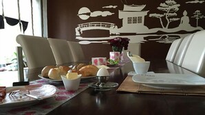 Una mesa de comedor con un mural tradicional japonés, una selección de pasteles y un pequeño jarrón con flores.