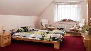 Un dormitorio con una cama, dos sillas, una mesita, una lámpara y una ventana con cortinas.