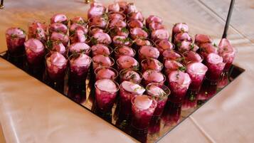 Una bandeja con vasos llenos de una bebida rosada, adornada con hierbas, sobre una superficie reflectante.