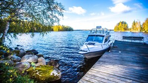 A boat docked at a wooden pier with a forested shoreline in the background. - Hotel PajarinHovi (Kitee)