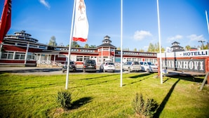 A hotel with a red and white facade, multiple flags, and a parking lot with several cars. - Hotel PajarinHovi (Kitee)