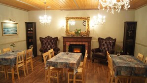 A dining room with wooden tables and chairs, a fireplace, and ornate chairs. - Hotel PajarinHovi (Kitee)