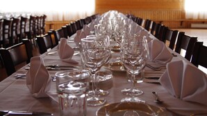A long dining table set with multiple wine glasses, plates, and cutlery, surrounded by chairs. - Hotel PajarinHovi (Kitee)
