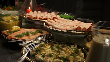 A buffet table with various dishes, including salmon, rolls, and a casserole, with serving utensils and a candle in the background.