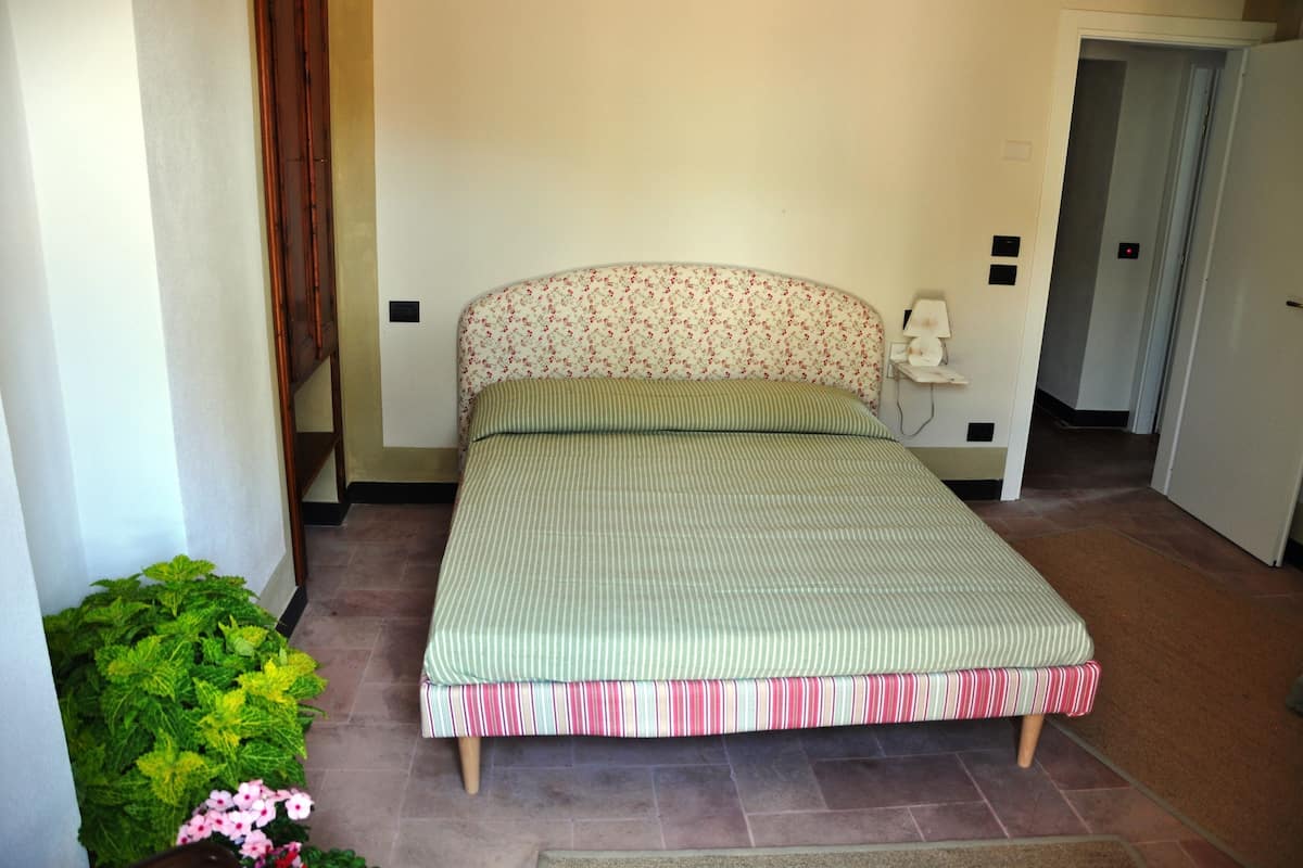 A small, single-bed room with a floral headboard, a bedside table, and a small window.