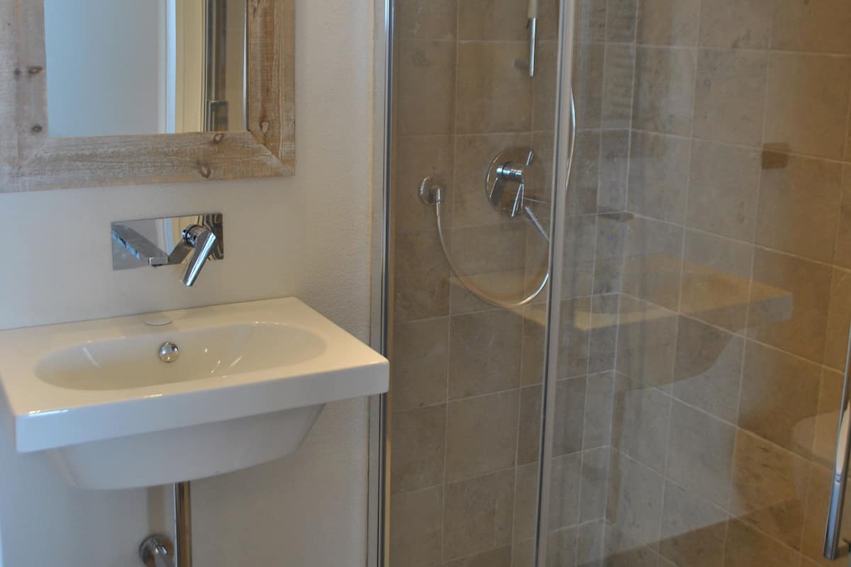 A bathroom with a glass-enclosed shower, a sink with a mirror above it, and patterned tiles on the walls.