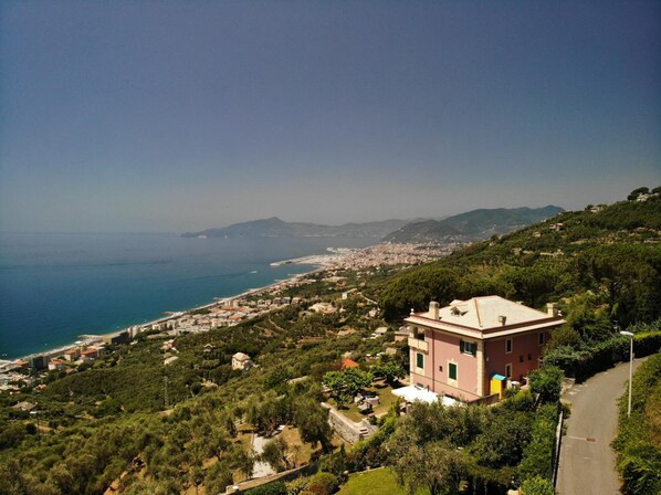 A coastal town with a prominent pink building surrounded by greenery and a view of the sea. - Olivenere Villa Agriturismo (Lavagna)