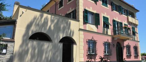 A multi-story building with a pink facade, green shutters, and a stone base.