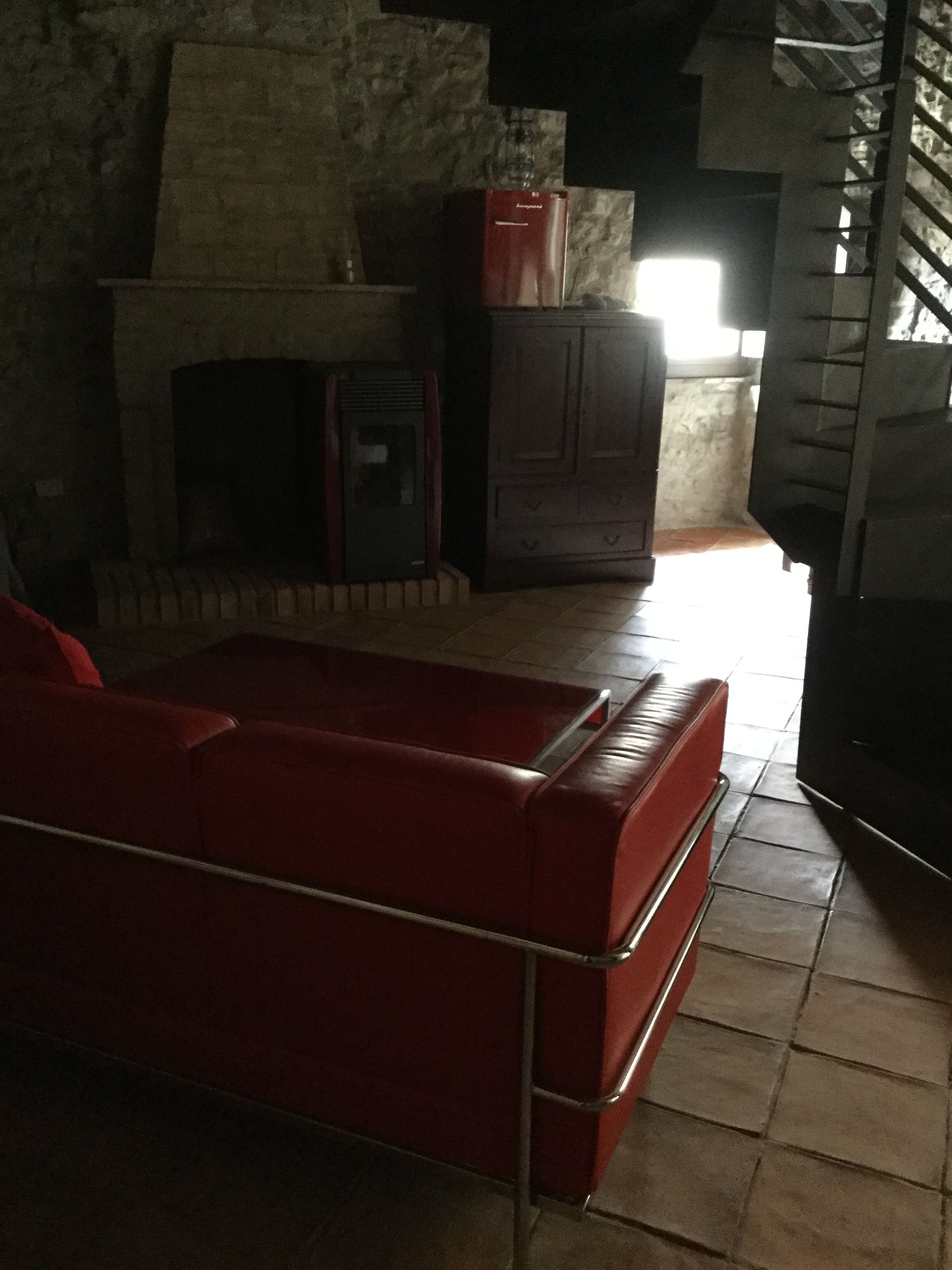 A room with a red sofa, a fireplace, a stone wall, and a window.
