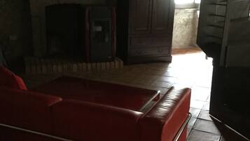 A room with a red sofa, a fireplace, a stone wall, and a window.