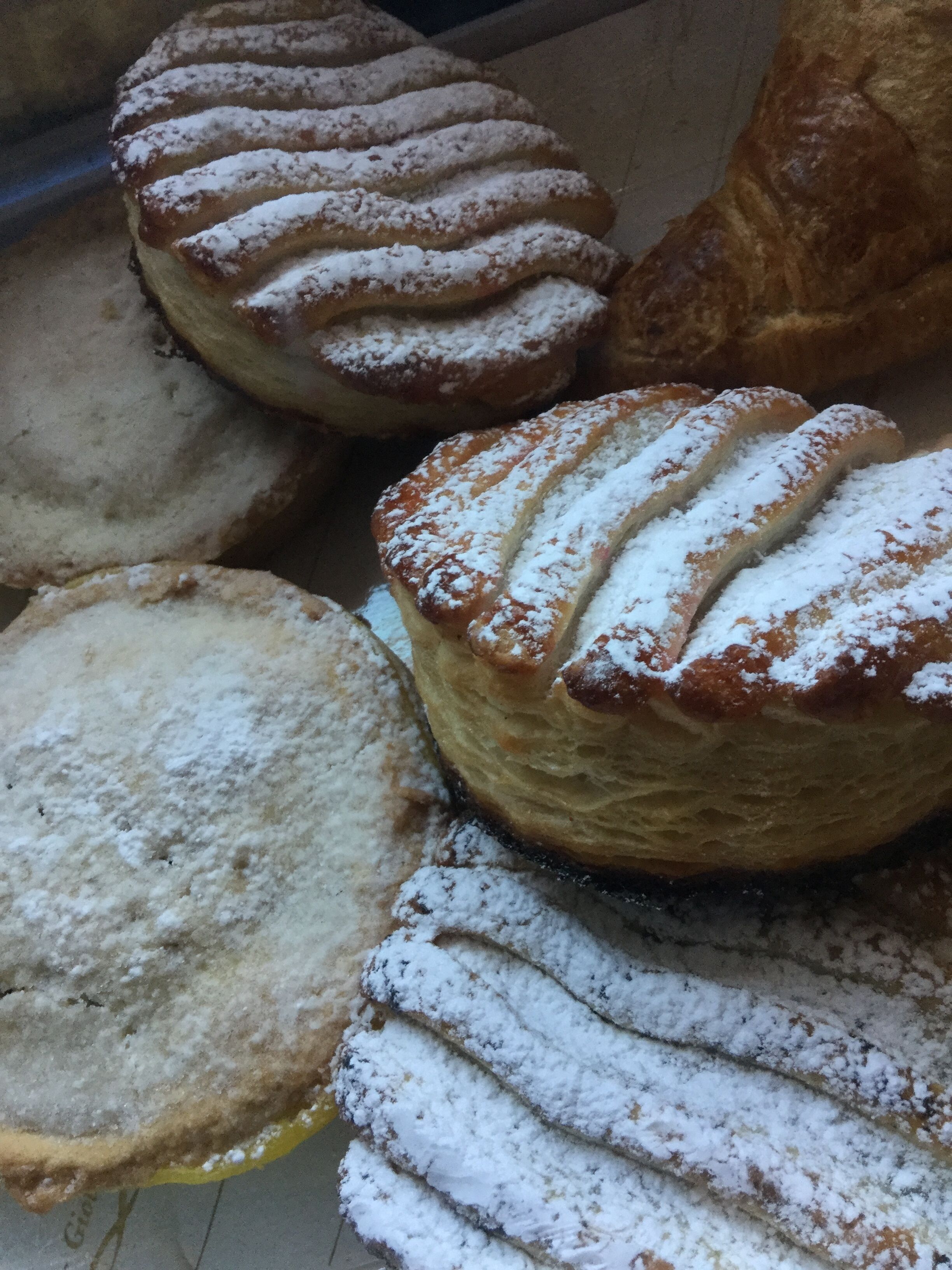 Un assortiment de viennoiseries, notamment des pâtisseries feuilletées et des croissants, saupoudrés de sucre glace.