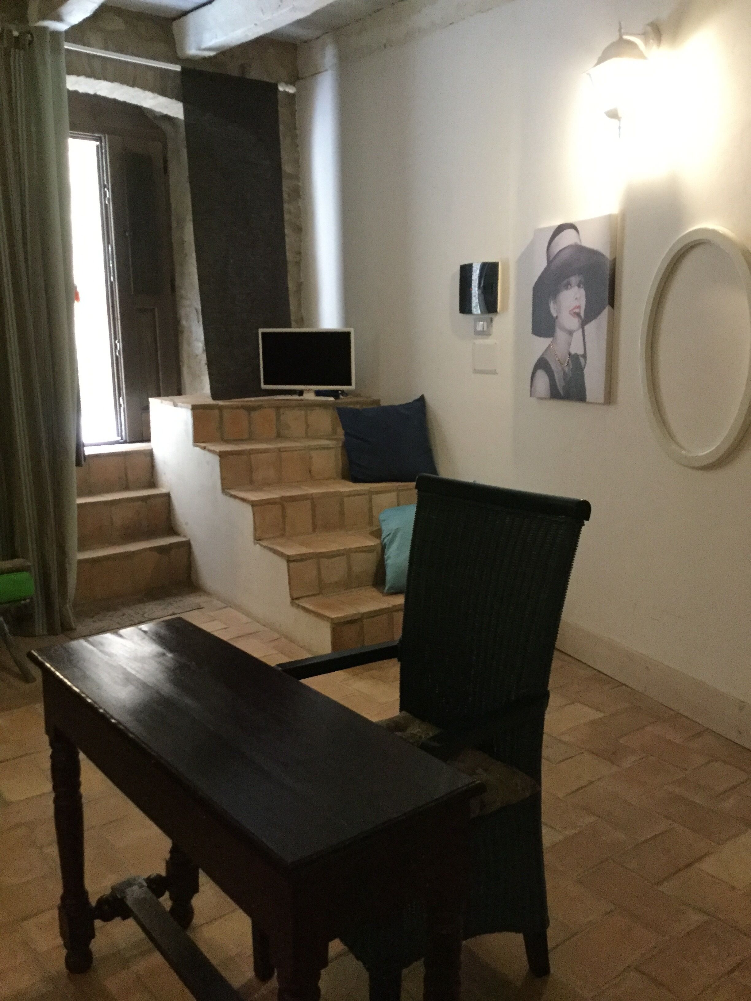 A room with a wooden table, a chair, a staircase, a flat-screen TV, and a framed picture on the wall.