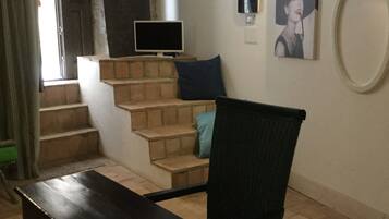 A room with a wooden table, a chair, a staircase, a flat-screen TV, and a framed picture on the wall.