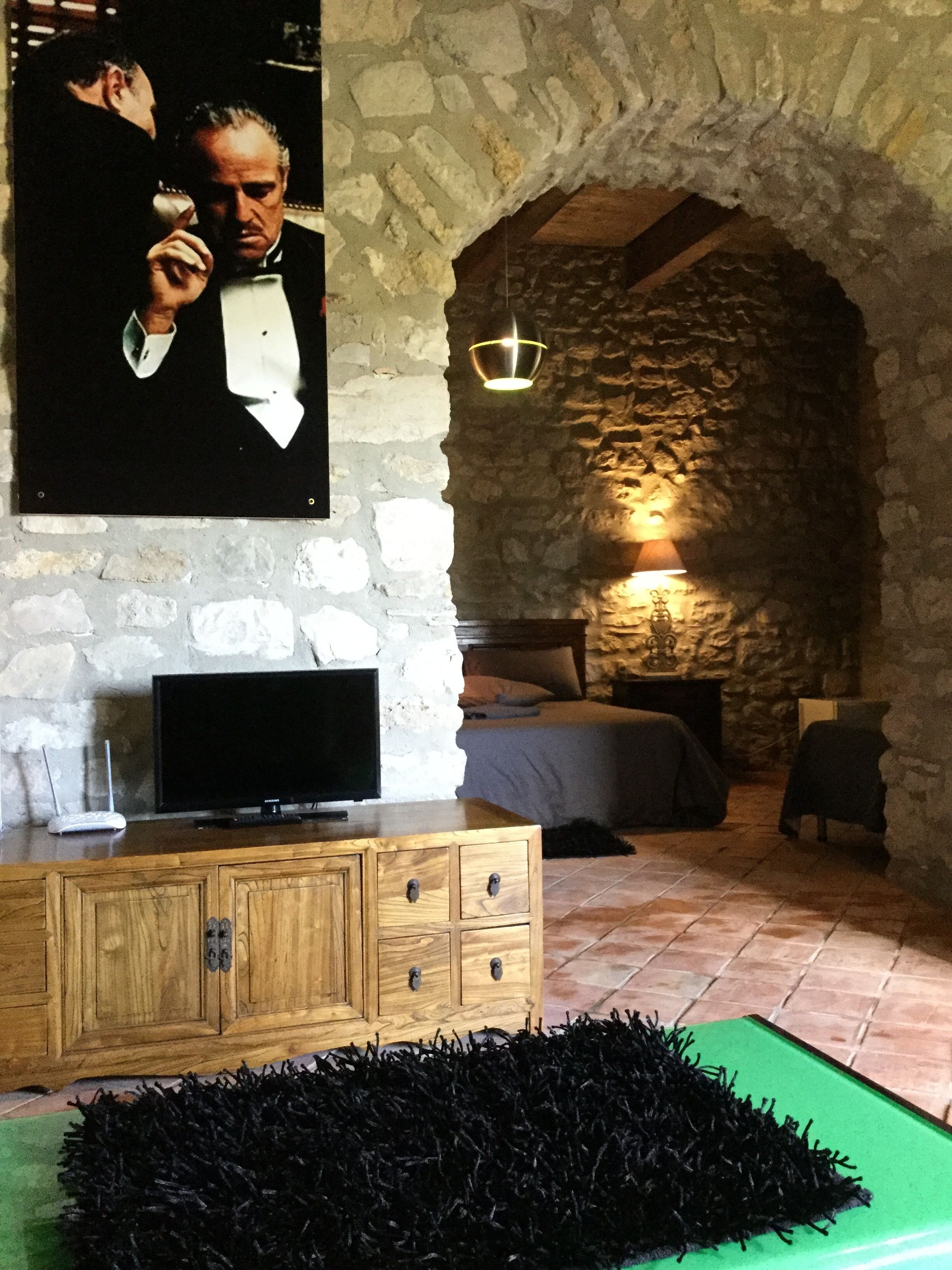 A room with a stone wall, a wooden cabinet, a television, a bed, and a green rug.