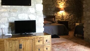 A room with a stone wall, a wooden cabinet, a television, a bed, and a green rug.