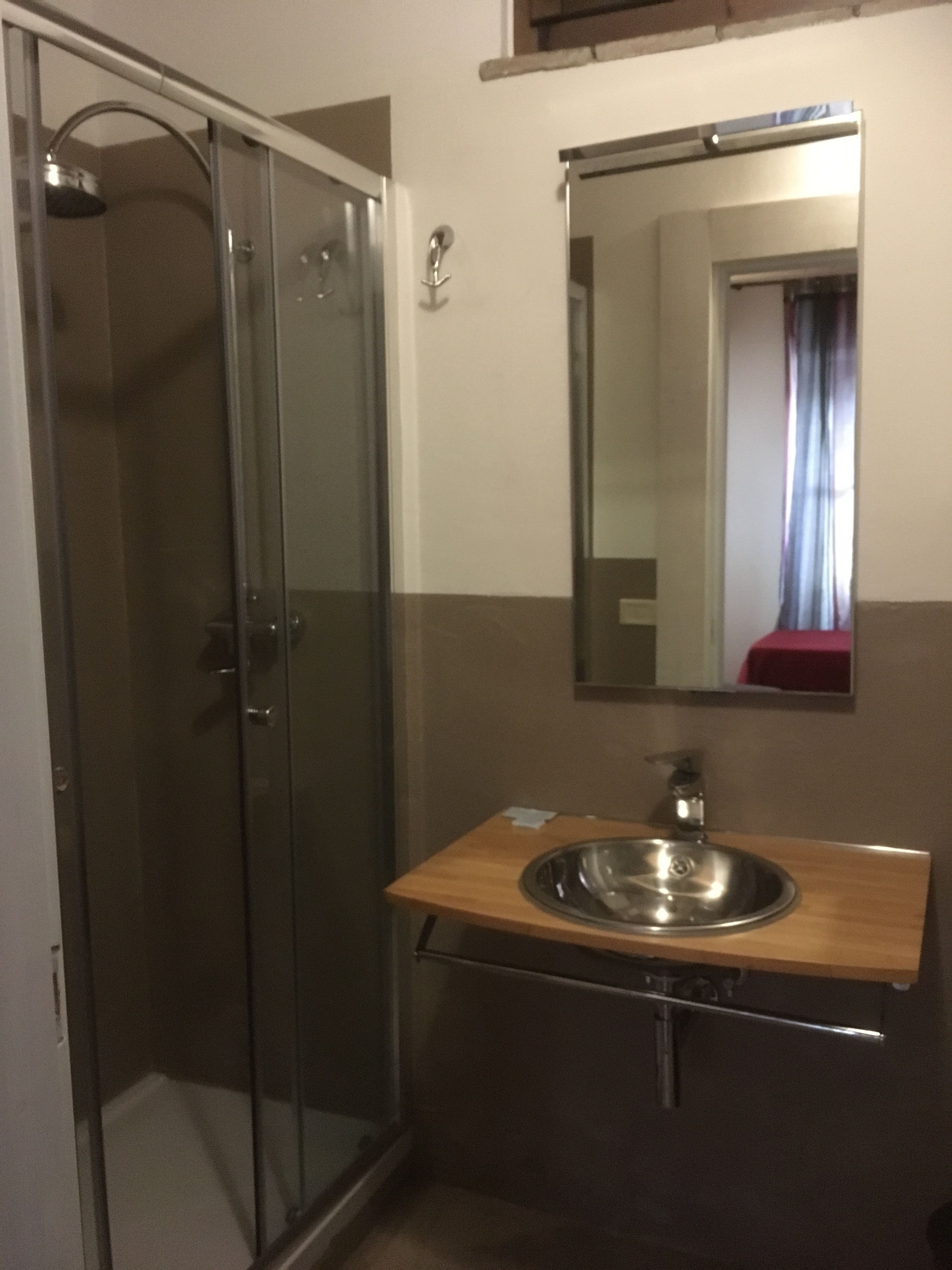 Une salle de bain dotée d’une douche à parois de verre, d’un meuble-lavabo en bois avec un évier en acier inoxydable et d’un miroir au-dessus de l’évier.