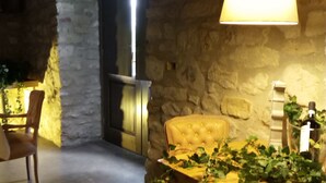 A cozy room with a stone wall, a wooden chair, a table with a lamp, and a bottle on the table.