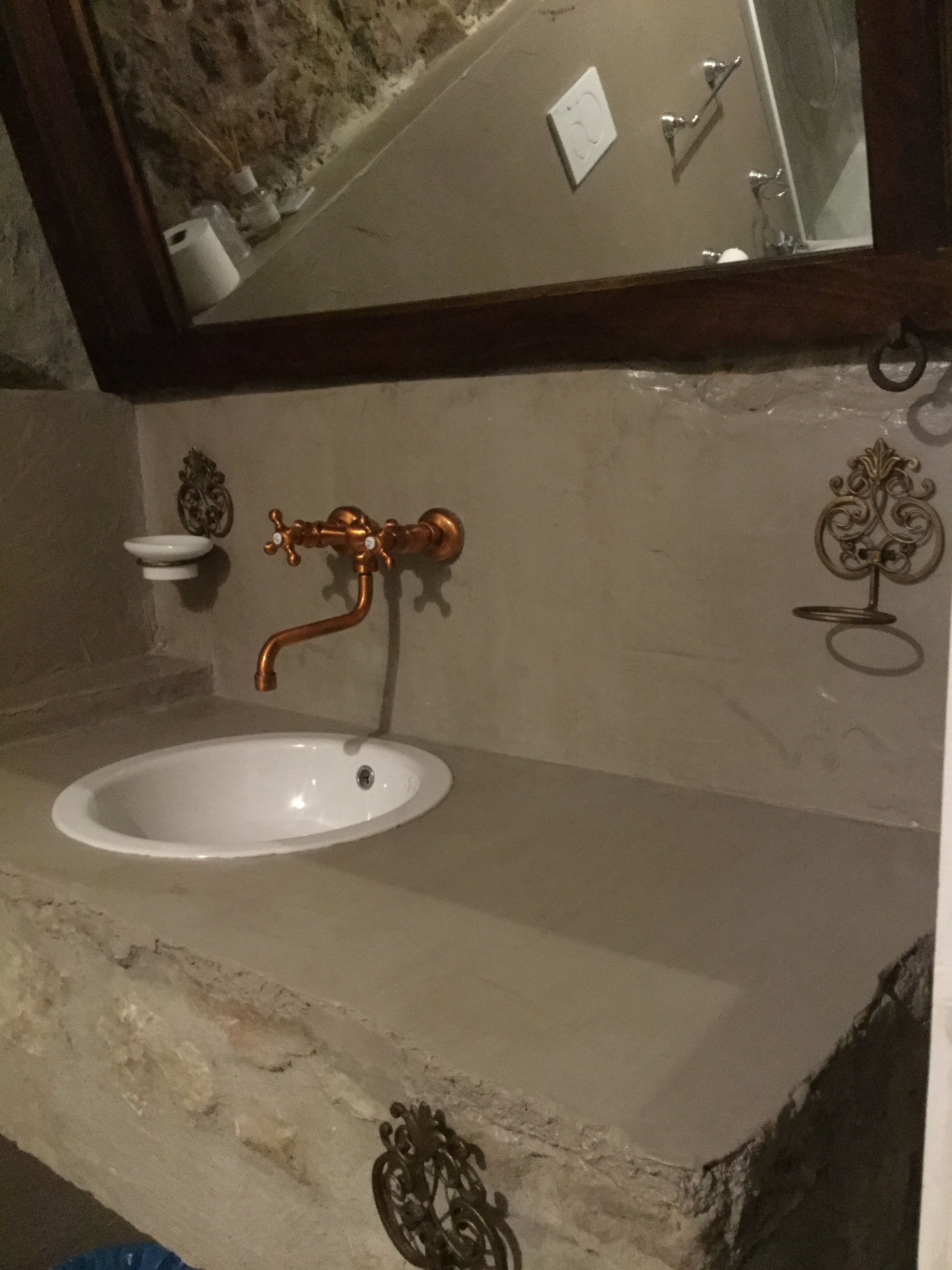 A bathroom with a white sink, a copper faucet, and decorative wall sconces.