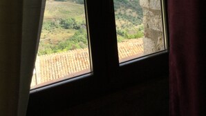A window with a view of a stone wall and a landscape with greenery and a tiled roof.
