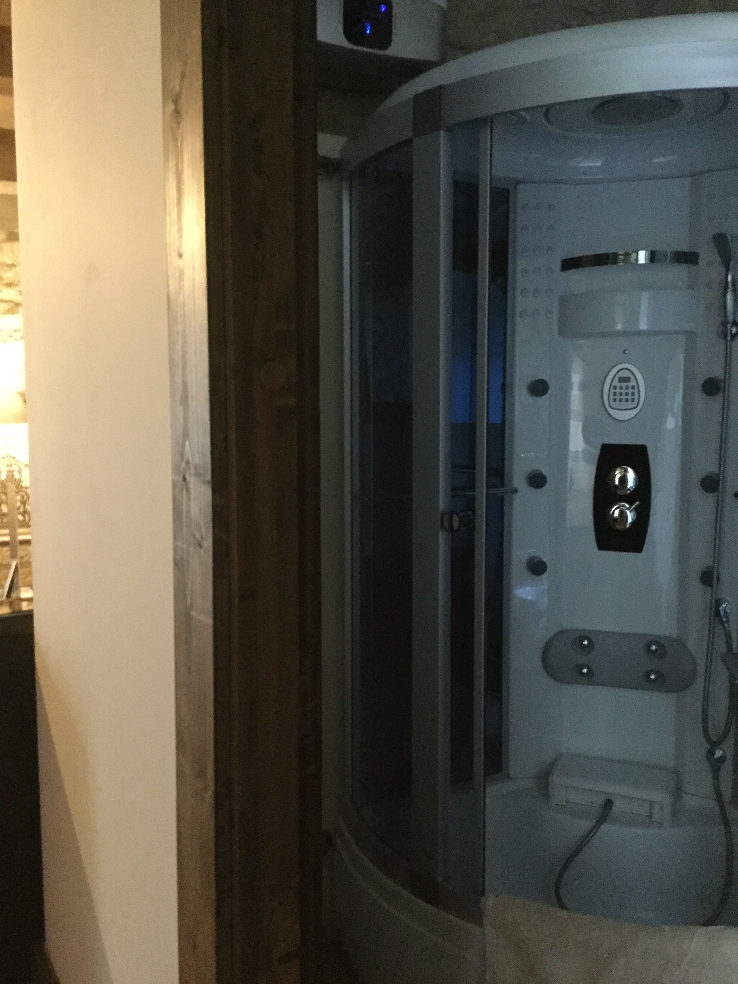 A modern bathroom with a glass-enclosed shower, a control panel, and a visible water outlet.