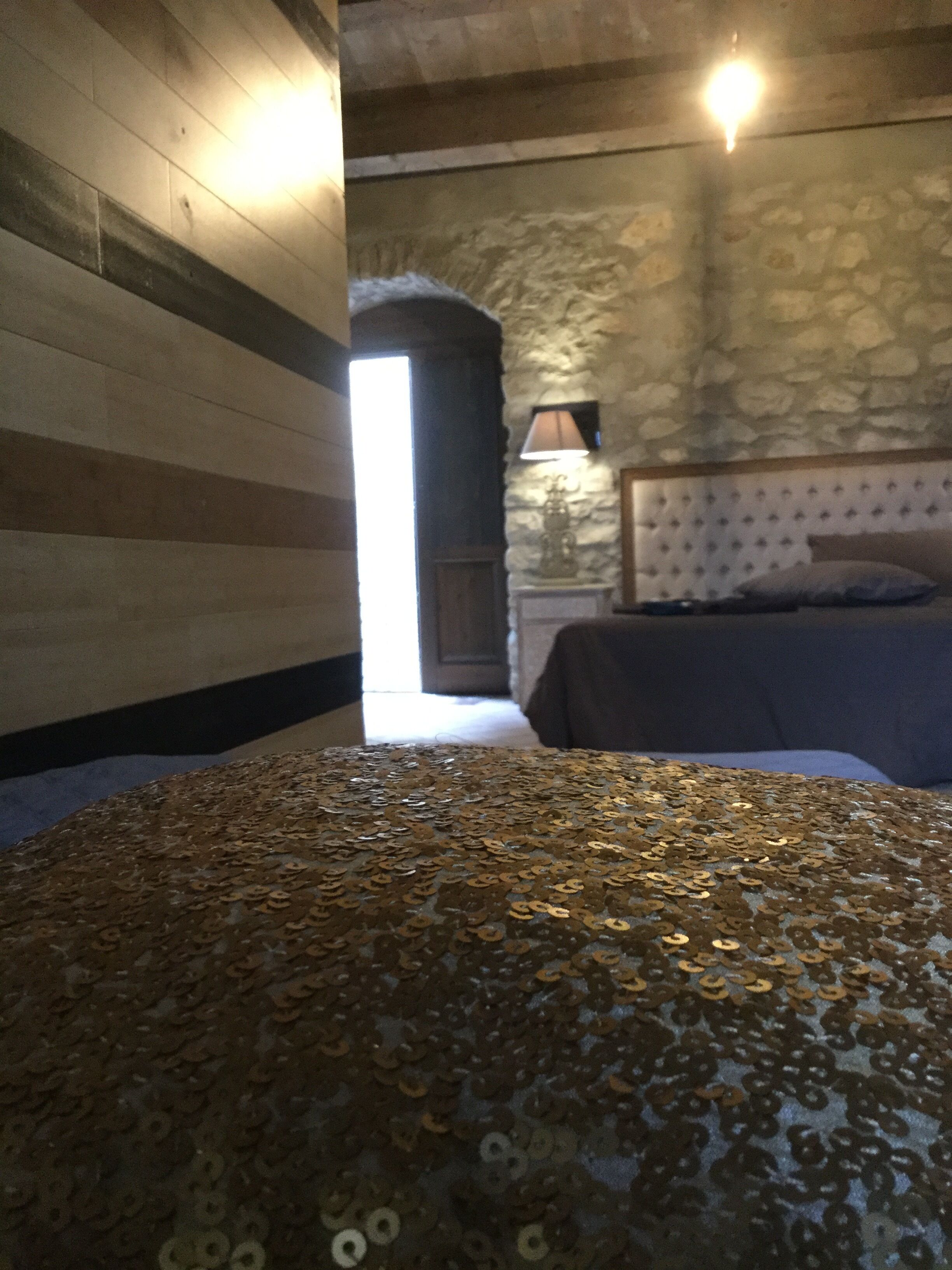 Ein Zimmer mit einem Bett, das mit goldfarbenen Pailletten besetzt ist, einer Steinsäule und einer Holzbalkendecke.