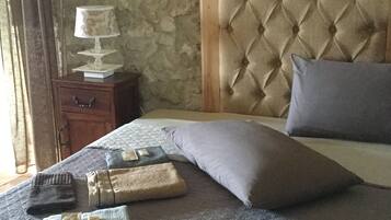 Ein ordentlich bezogenes Bett mit einer gebügelten Zierkopflehne, ein Nachttisch mit einer Lampe und ein Fenster mit Vorhängen.