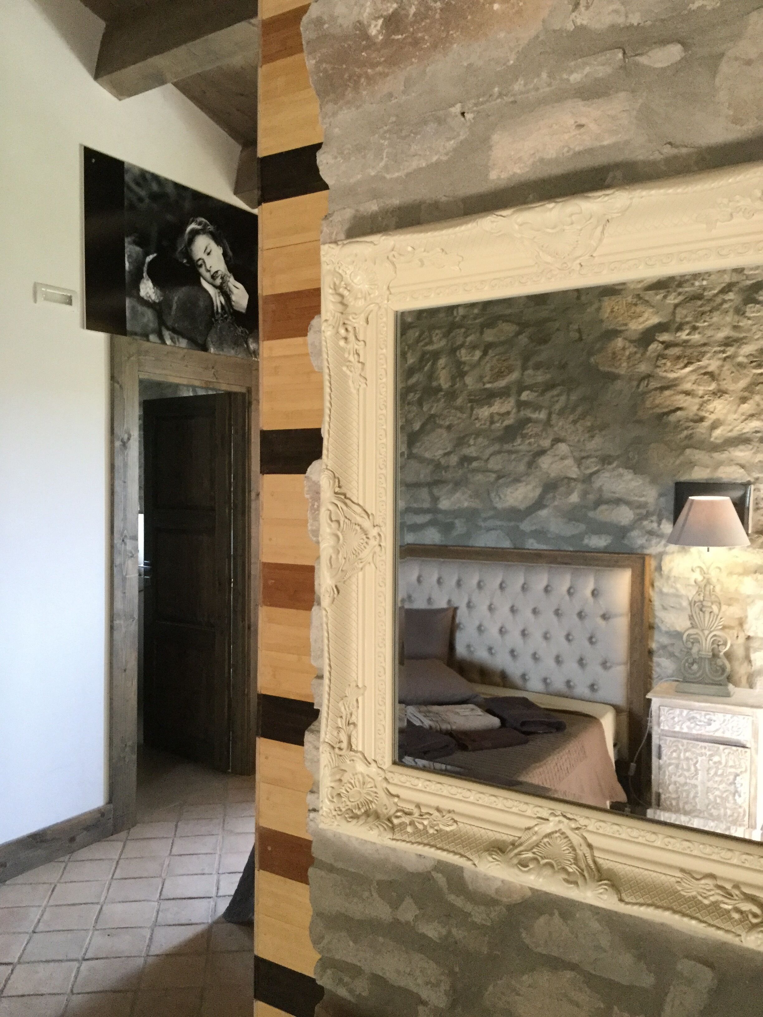 Una habitación con pared de piedra, una cama con cabecera capitonada, una mesita de noche con lámpara y un cuadro enmarcado en la pared.