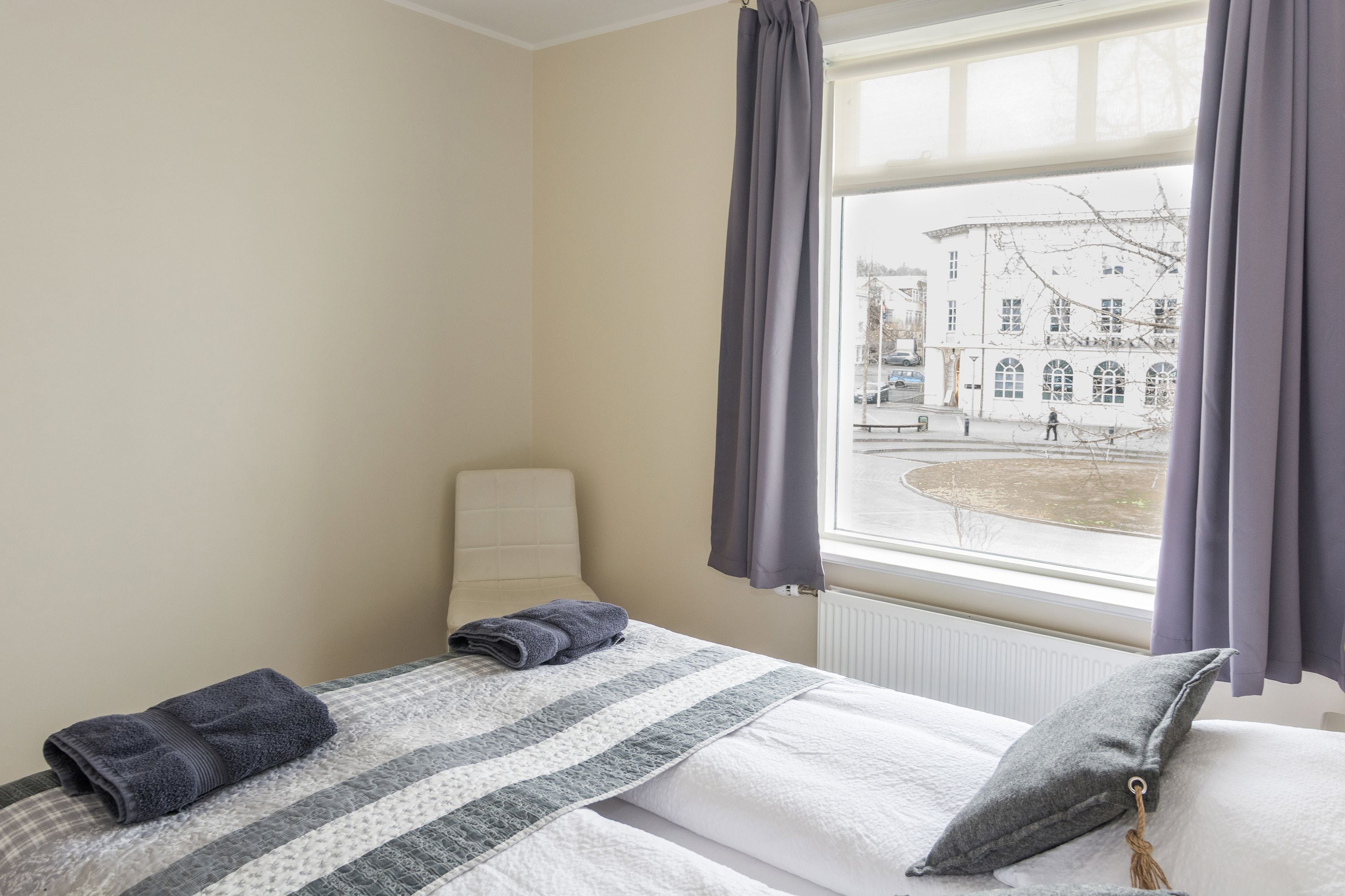 A hotel room with a bed, a chair, and a window with curtains.