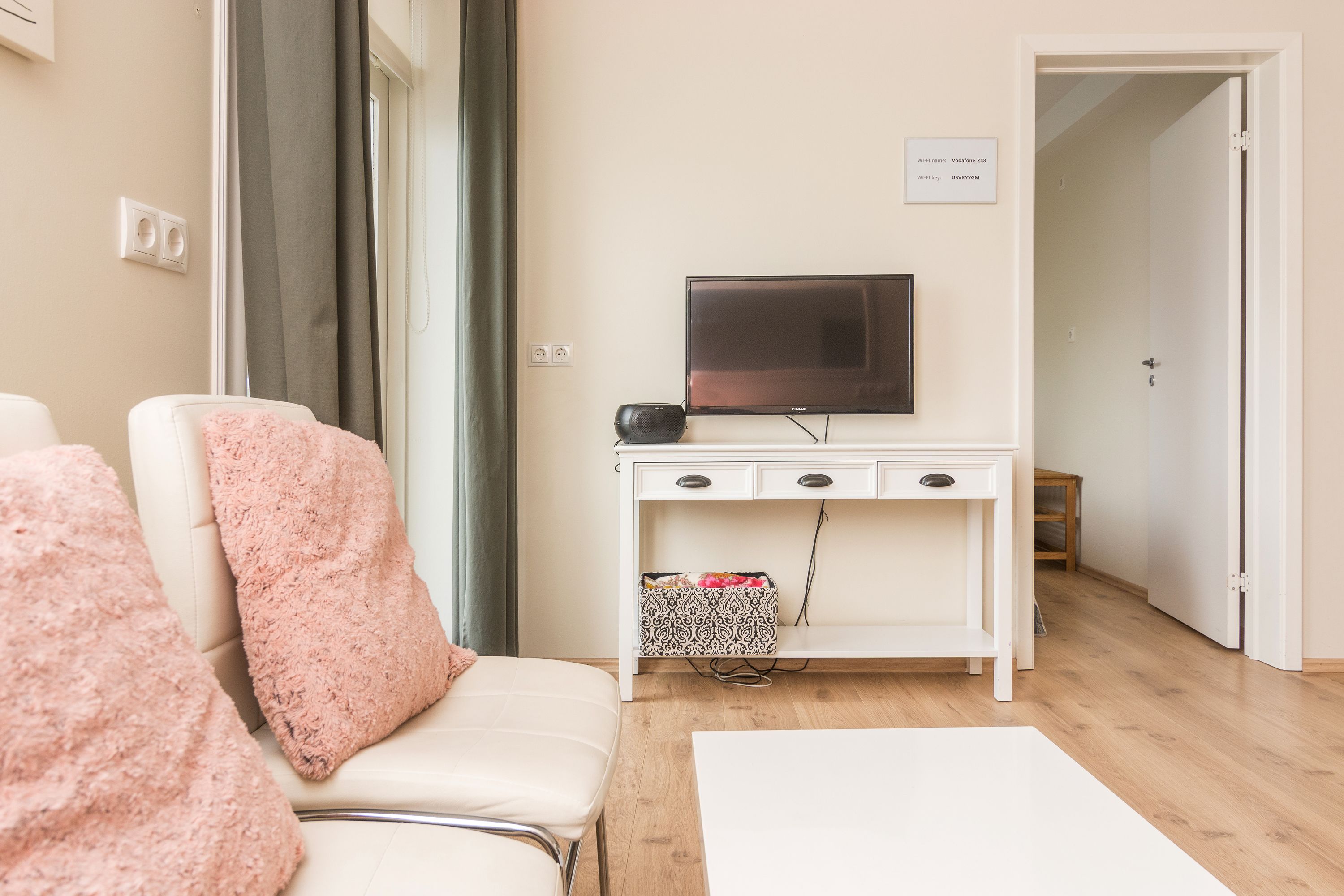 A modern living room with a white sofa, a television on a white cabinet, and a wooden floor.