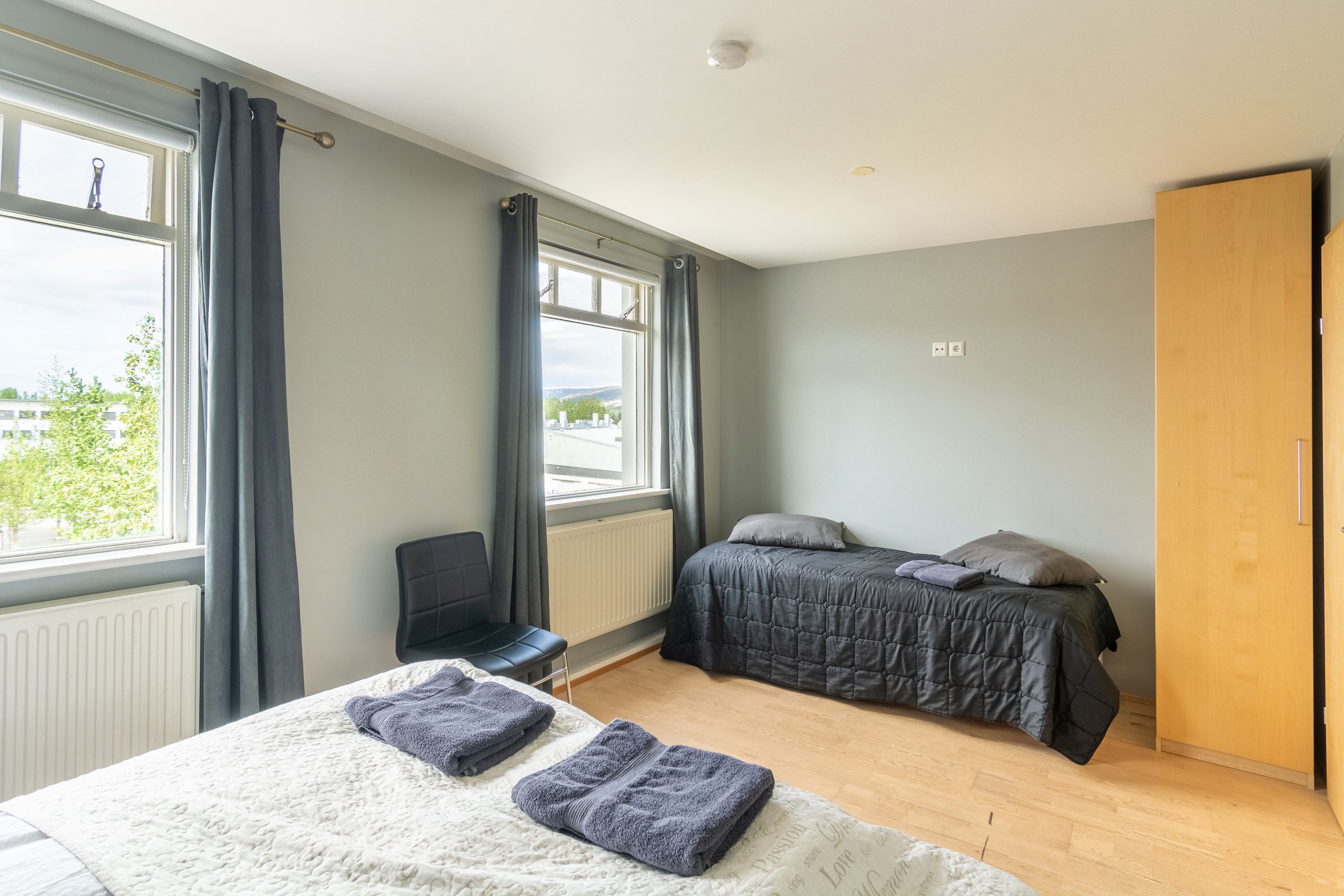 Un dormitorio con dos camas, una silla, un armario de madera y una ventana con cortinas.