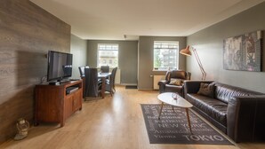 A modern living room with a wooden entertainment unit, a leather sofa, a coffee table, and a city-themed rug.