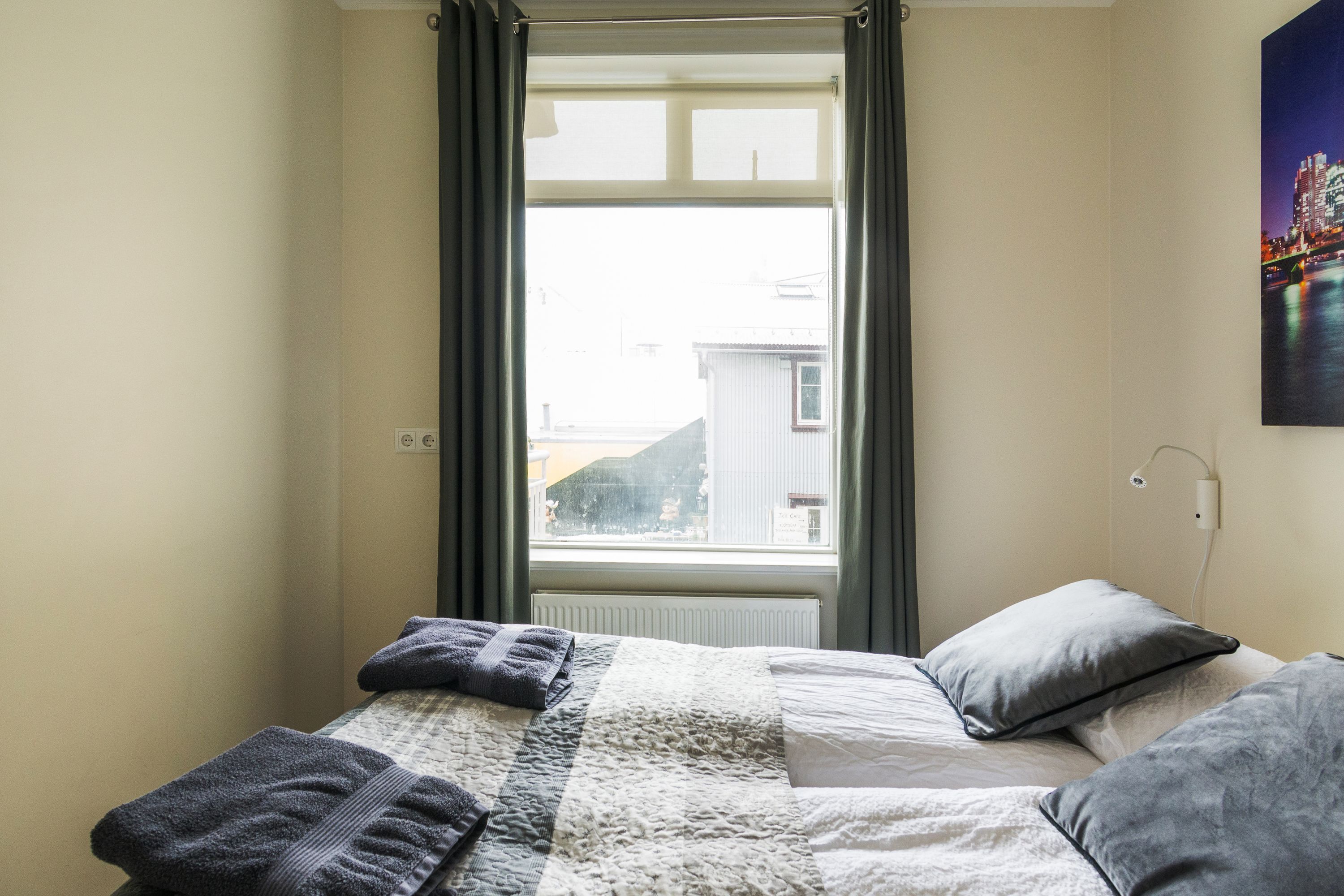 Une chambre à coucher avec un lit, deux oreillers, une couverture et une fenêtre avec des rideaux.