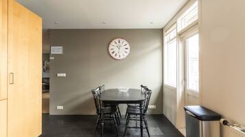 Un comedor con una mesa redonda y sillas, un reloj de pared y un cubo de basura.