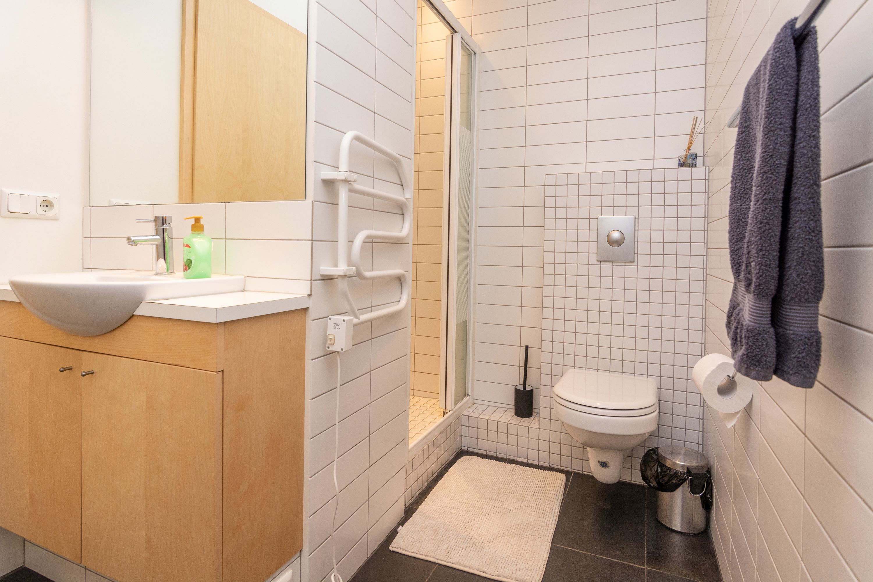 Une salle de bain moderne avec un lavabo blanc, un meuble-lavabo en bois, une douche avec une porte en verre, des toilettes et un porte-serviettes.