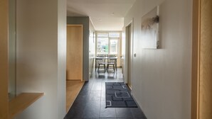 A hallway with a dark rug, wooden flooring, and a dining area with chairs and a table in the background.