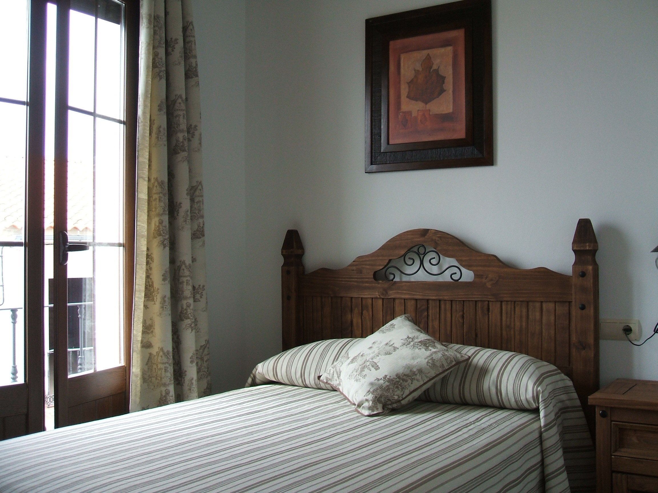 Un dormitorio con cabecera de madera, cama con ropa de cama a rayas, un cuadro en la pared y una ventana con cortinas.