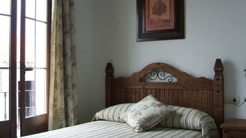 Un dormitorio con cabecera de madera, cama con ropa de cama a rayas, un cuadro en la pared y una ventana con cortinas.