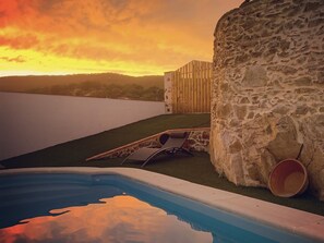 A swimming pool with a stone wall and a wooden fence in the background. - Casa Rural Sierra Tórtola (Hinojales)